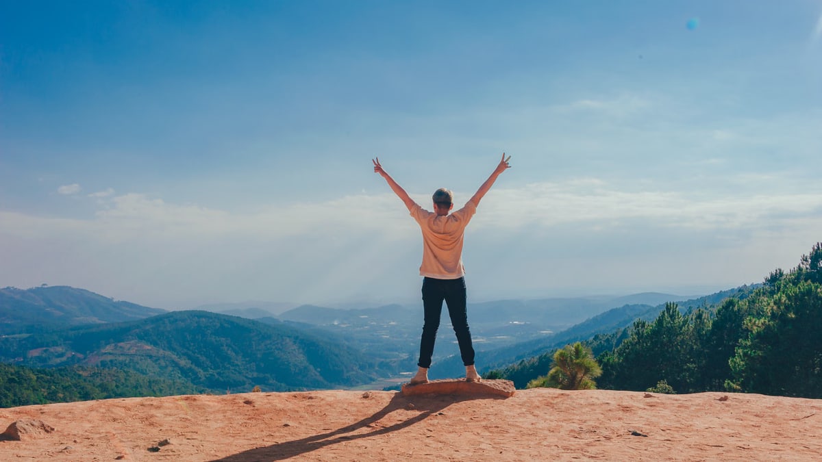A woman stands victoriously on a mountain top with arms raised, embracing nature and freedom.